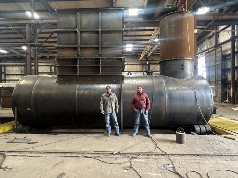 Two men standing in front of an industrial tank